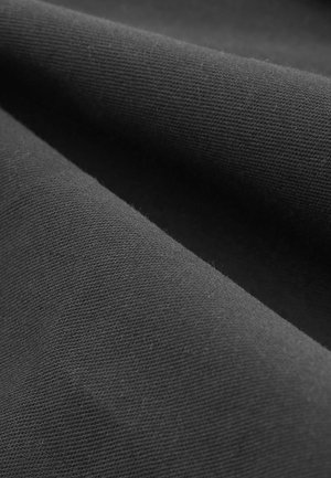 Tejido de algodón negro con una textura suave, que muestra una ligera elasticidad y un patrón finamente tejido, doblado para mostrar profundidad y suavidad.