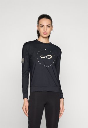 Black long-sleeve top with a round neckline, featuring a central infinity symbol design and branded sleeve patch. Paired with black leggings.