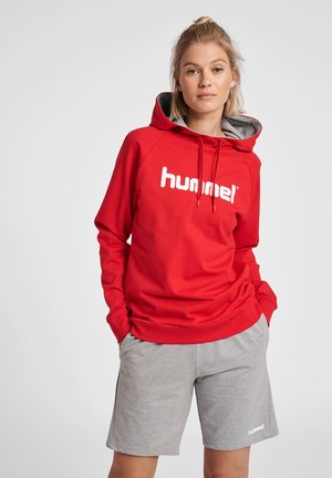 Rode hoodie met een wit logo, gecombineerd met grijze shorts. De hoodie heeft trekkoorden en een zachte textuur.