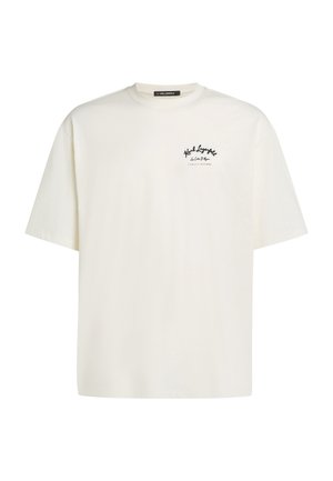 T-shirt à manches courtes couleur crème avec une coupe ample, présentant un logo noir imprimé sur la poitrine gauche. Confectionné en tissu de coton doux.