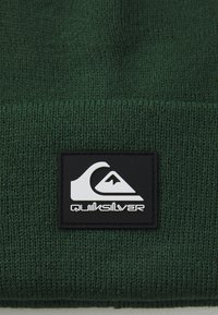 Beanie lavorato a maglia verde con una toppa in gomma nera che presenta un logo bianco di un'onda e una montagna, tessuto testurizzato e orlo arrotolato.