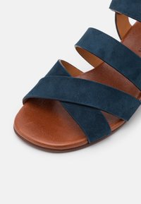 Sandale à bout ouvert avec semelle en cuir marron et brides croisées en daim bleu marine sur le pied.
