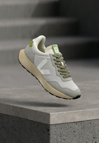 Αθλητικό παπούτσι σε ανοιχτό γκρι και πράσινο με υφασμάτινο επάνω μέρος με υφή, αντιθετική λαστιχένια σόλα και εμφανές λογότυπο στο πλάι και στη γλώσσα.