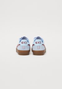Nike sneakers i lys blå ruskind med mørkerøde detaljer, en gummibrown sål og broderet "NIKE" branding på hælen.