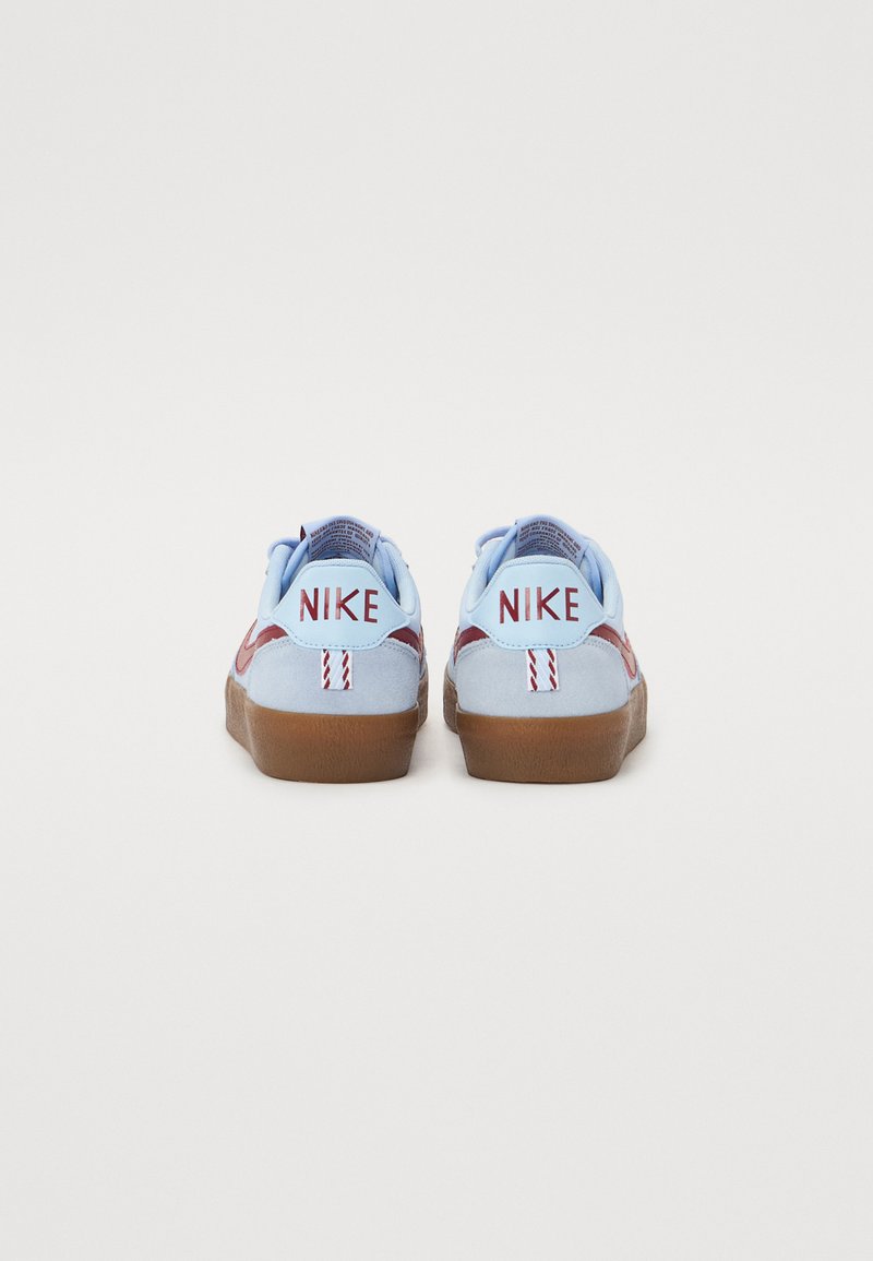 Nike sneakers van lichtblauw suede materiaal met donkerrode accenten, een rubberen bruine zool en geborduurde "NIKE" branding op de hiel.