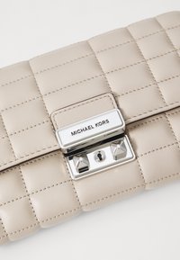 Beige Leder-Clutch mit gestepptem Muster, silberfarbener Hardware, einem Logo-Schild und dreieckigen Nieten. Verfügt über einen Verschluss mit Riegel und Nähedetails.