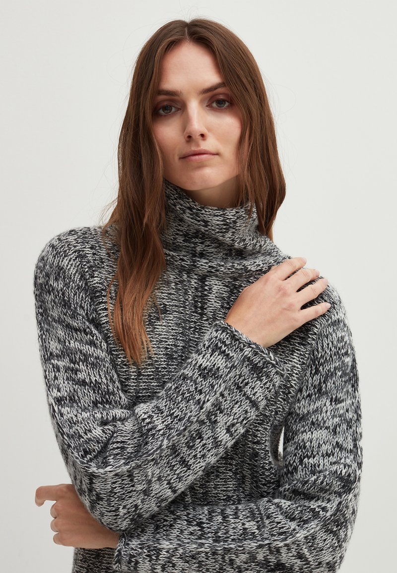 Kuscheliger Rollkragenpullover mit einem schwarz-weißen, gesprenkelten Strickmuster. Lockere Passform mit weiten Ärmeln und strukturiertem Stoff, der über ribbelige Bündchen verfügt.