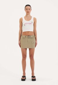 Bílý crop top s vyšitým vzorem, v kombinaci s khaki mini sukní s opaskem v pase a dvěma předními kapsami. Černé platformové sandály.