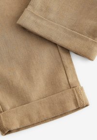 Gros plan sur un tissu en lin marron clair avec ourlets pliés et détails de couture visibles sur une paire de shorts.