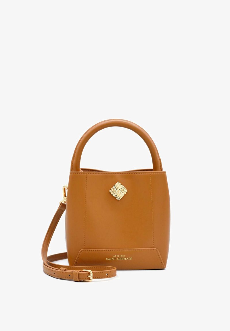 Brown leather handbag with a structured shape, circular handle, gold hardware accent, and removable shoulder strap, featuring logo detail at the base.