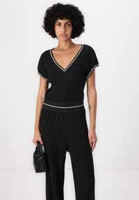 Svartstripet jumpsuit med V-hals, korte ermer, innsnevret midje og vide ben, akkompagnert av metalltråder.