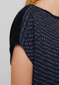 Mörkblå topp med ett blommönster i vitt och lila. Korta ärmar med en mjuk textur och en avslappnad passform.