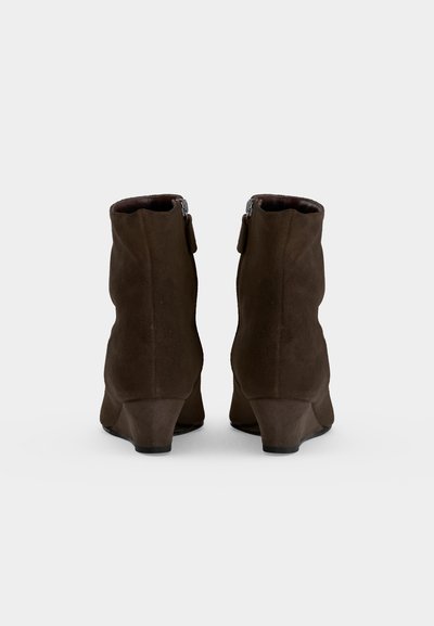 Paire de bottines en daim brun foncé avec petits talons compensés et fermetures éclair à l'arrière sur fond blanc.