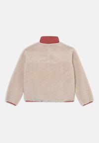 Fleecejakke i beige med rød krave, med en myk tekstur og en kroppsnær passform.Sømdetaljer er synlige over ryggen.
