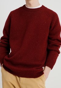 Punainen neulepusero, jossa on ribbireunainen pyöreä kaula-aukko, raglan-hihat ja kirjavuus. Rentoa istuvuutta, jossa on paksut hihansuut ja helma.