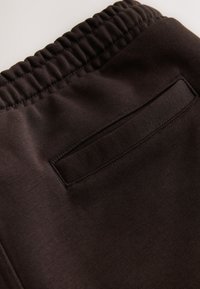Primer plano de cintura elástica negra y bolsillo trasero con apertura en pantalones o pantalones cortos de tela oscura.