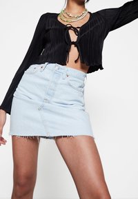 Haut court noir plissé avec lien à nouer à l'avant, associé à une mini-jupe en denim bleu clair avec ourlet effiloché et design à cinq poches.