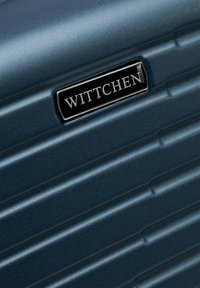 Valigia rigida di colore blu navy con design a strisce testurizzate, dotata di una placca in metallo nero con il logo "WITTCHEN". Finitura liscia.