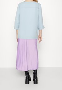 Jasnoniebieska bluzka z długim rękawem o strukturalnym wykończeniu, zestawiona z lejącą lawendową spódnicą midi. Czarne botki na wysokim obcasie do kolan.