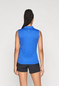 Bezrūpa zila polo krekls no viegla, strukturēta auduma ar apkakli un mazu logo aizmugurē, apvienots ar melniem šortiem.