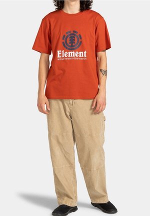 Rotes Baumwoll-T-Shirt mit einem runden Aufdruck mit dem Wort "Element" und erdigen Symbolen, kombiniert mit beigen, locker sitzenden Cargohosen.