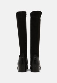 Botas negras hasta la rodilla con puntera de cuero liso y tacón grueso, con parte superior de ante y cierre de cremallera en la parte posterior.