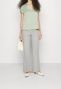 Mintgrön blus med korta ärmar och krage, i kombination med ljusgrå utsvängda byxor. Tillbehören inkluderar en liten vit handväska och beige skor.