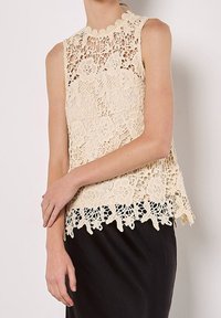 Haut en dentelle beige avec motifs floraux, encolure festonnée et design en couches. Présente une coupe ample et un ourlet contrastant.
