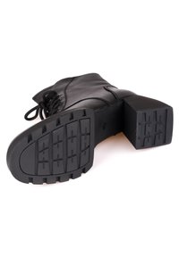 Botte noire en cuir avec semelle épaisse à crampons et talon bloc, lacée à l'avant, photographiée vue côté semelle.