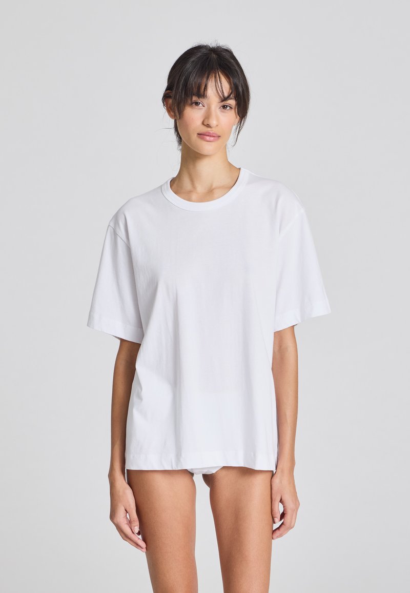 Tricou alb din bumbac, cu o croială lejeră, mâneci scurte și decolteu rotund, având o textură netedă și fără modele vizibile.