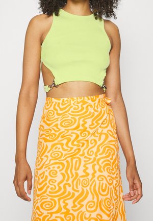 Grøn ribbet crop top med sideudskæringer, sikret med metalliske kroge, kombineret med et livligt orange skørt med et abstrakt swirl-mønster.
