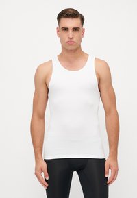 Hvid tanktop lavet af blødt, ribbet bomuld. Har brede stropper og en rund halsudskæring. Bæres med sorte tætsiddende bukser.