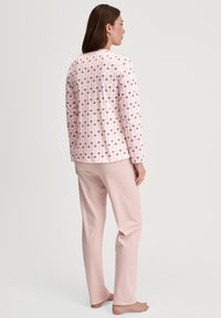 Roze pyjama set met een langetermijn top met een patroon van kleine paarse bloemen, gecombineerd met effen roze broeken. Zachte katoen stof.
