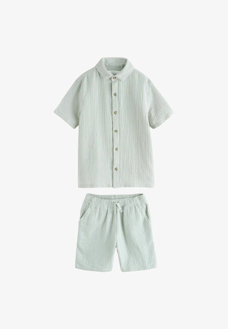 Chemise à manches courtes vert clair avec boutons et short à taille élastique, tous deux fabriqués dans un tissu texturé léger avec de fines lignes verticales.