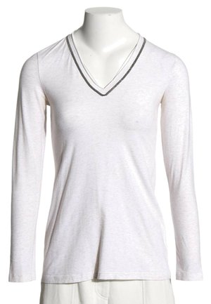 Camiseta blanca de manga larga con cuello en V y ribete oscuro en el cuello, mostrada en torso de maniquí sin cabeza.