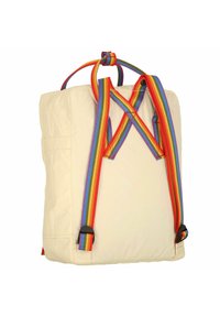 Béžový batoh s pásky v duhových pruzích, čtvercového tvaru, vyrobený z látky, má stahovací uzávěr a černé kovové doplňky.