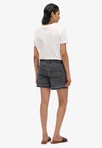 Shorts en denim noir avec ourlet effiloché et poches arrière, accompagnés d'un t-shirt en coton blanc. Les chaussures décontractées sont des sandales à glissière noires.