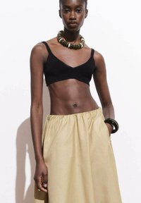 Crni skraćeni bralet u kombinaciji s khaki suknjom visokog struka. Model nosi debele perle kao ogrlicu i narukvicu na zapešću.