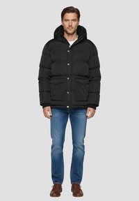 Sort dunjakke med hætte, med quiltet design, trykknapper og to forlommer. Brugt med blå jeans og brune sko.