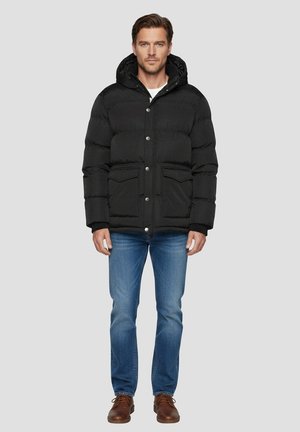 Sort dunjakke med hætte, med quiltet design, trykknapper og to forlommer. Brugt med blå jeans og brune sko.