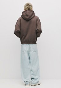 Felpa oversized marrone con cappuccio, abbinata a jeans baggy azzurri chiari. Tessuto morbido, vestibilità rilassata e dettagli di cucitura minimi.
