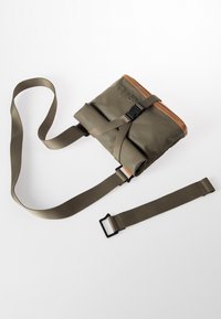 Borsa impermeabile verde con accenti in pelle marrone, tracolla regolabile, chiusura con fibbia e design con parte superiore ripiegabile. Texture liscia.