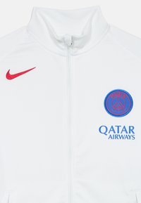 Veste zippée blanche avec col montant. Présente un logo Nike rouge, un blason du Paris Saint-Germain bleu et une marque Qatar Airways bleue. Texture lisse.