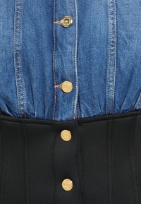 Jeans košulja s nabranim detaljima i zlatnim gumbima, koja prelazi u prilagođeni crni korzet s vertikalnim šavovima i odgovarajućim zlatnim gumbima.