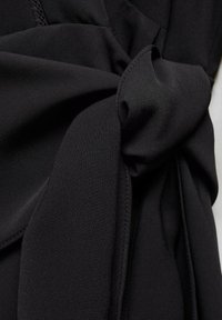 Black fabric featuring a knotted detail, smooth texture, and pleated design, with even stitching and a clean finish.