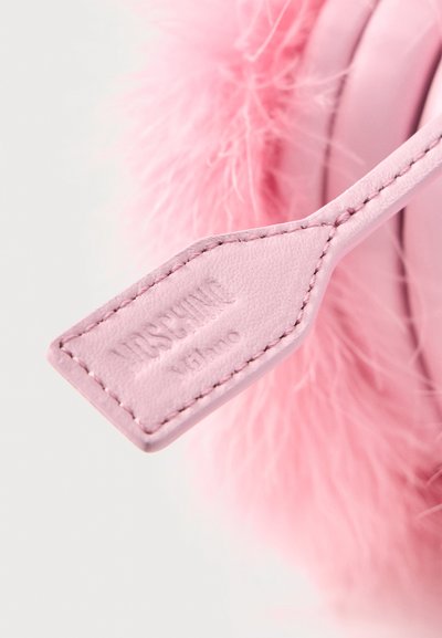 Ροζ λουρί τσάντας από δέρμα με ραμμένα άκρα και χαραγμένο λογότυπο "Moschino Milano", συνδεδεμένο σε φουσκωτό ροζ υφασμάτινο φόντο.