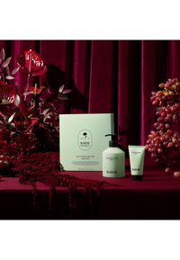 Babor Soul & Body Routine set met een lichtgroene lotionfles en een kleine wasbuis op een bordeauxvelours achtergrond met florale accenten.