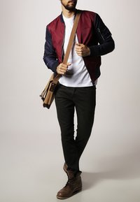 Skjortjacka i maroon och marinblått med ribbade mudd, vit t-shirt, svarta jeans och bruna läderkängor. Brun axelremsväska över kroppen.
