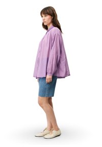 Lichtpaarse oversized button-up shirt met lange mouwen, gecombineerd met denim shorts en beige veterschoenen. Eenvoudig ontwerp, casual pasvorm.
