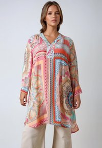 Tunique colorée à motifs avec décolleté en V, manches longues et imprimés décoratifs dans des tons de rose, bleu et crème ; tissu léger.